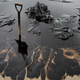 A shovel sits in oil-covered sand.